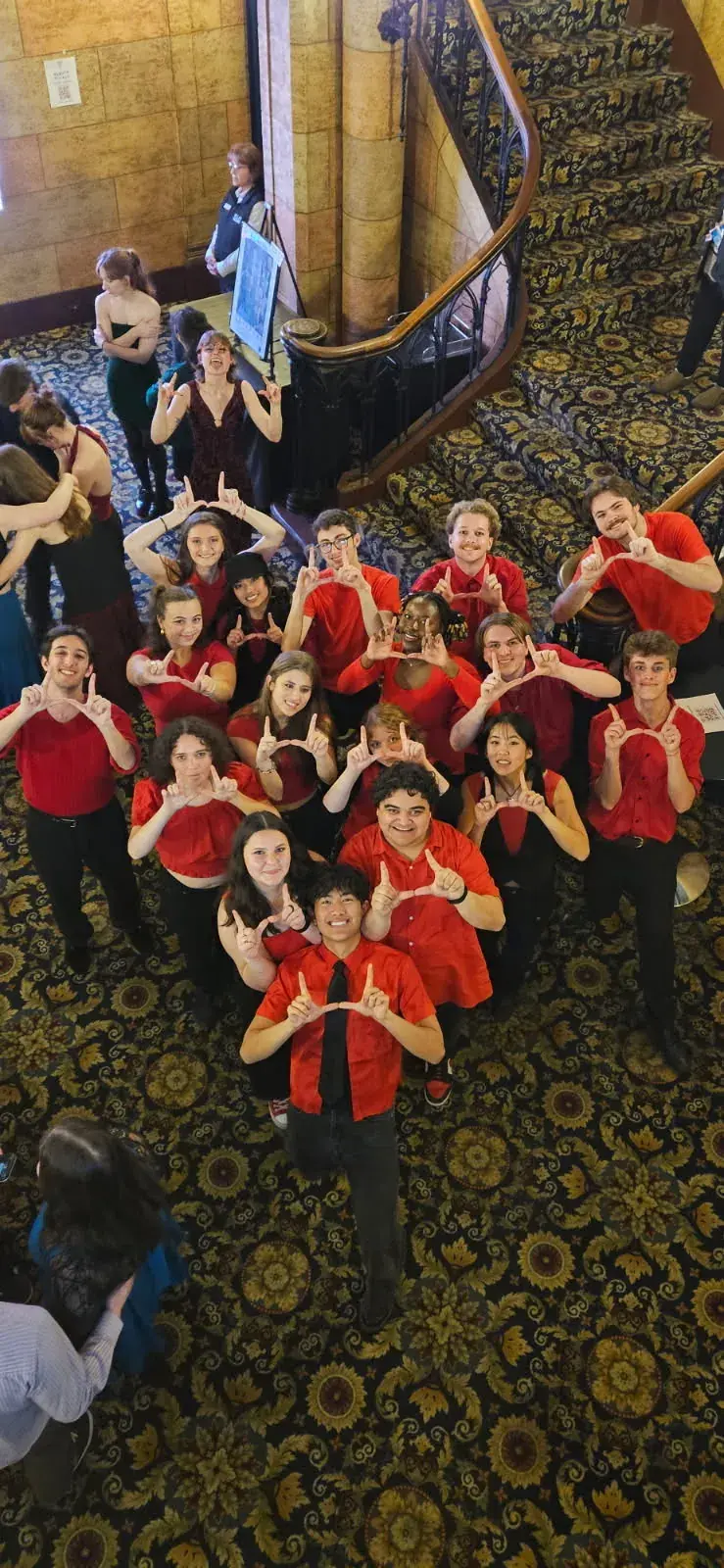 Salt Flats A Cappella in red throwing the U in a theater lobby on ICCA competition day